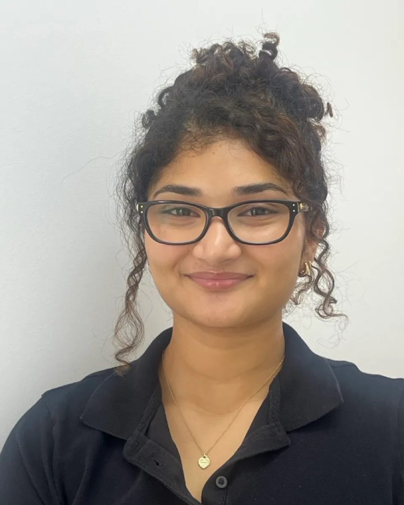 Headshot of physiotherapist Hazel John smiling in a black polo shirt and wearing glasses.