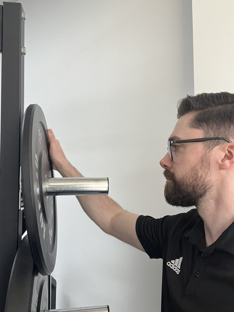 Physiotherapist loading a weight plate in the private gym at Spine & Dandy in Holland Park West